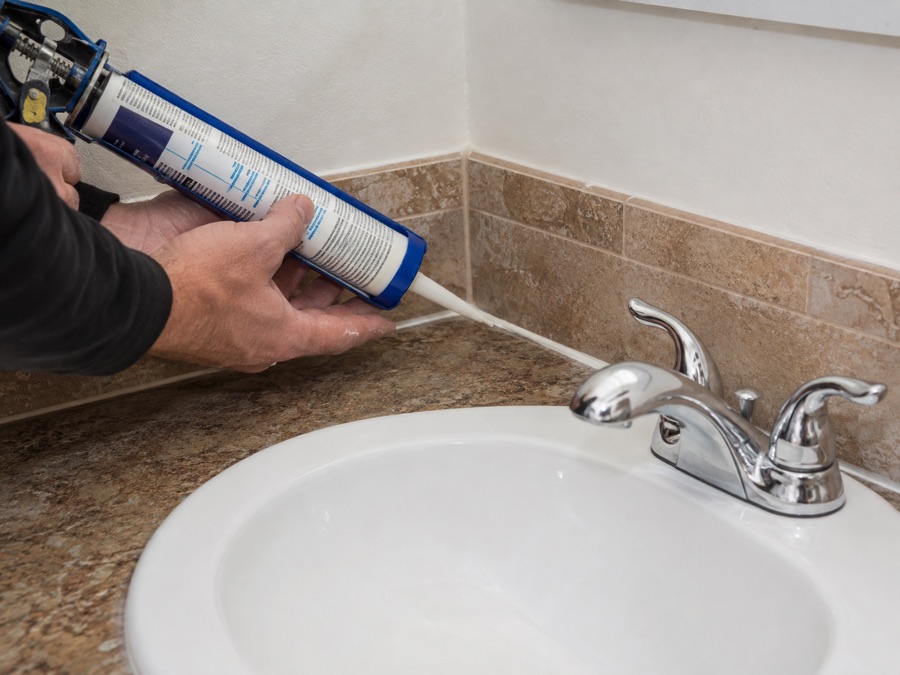 Applying fresh silicone caulking around a bathroom sink